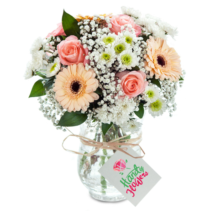 Evocative of Bexley's peaceful charm, this beautifully arranged bouquet brims with expertly selected blooms, united by a palette of inviting pastels. The central roses-full, peach-pink, and velvety-convey enduring sentiment, their unfurling petals glowing in the soft daylight. Two peach gerbera daisies, bold and uplifting, set a cheerful tempo against a cloud-soft mass of white baby's breath, infusing the arrangement with lightness. Small white chrysanthemums, each revealing a vivid green heart, add depth and a crisp coolness, nodding to the refreshing flora in Bexley's local green spaces. Eucalyptus leaves-deep green and lightly scented-are thoughtfully interspersed, their elongated forms lending both visual and aromatic contrast. Set within a clear, textured glass vase, every stem and drop of water is visible, underscoring the local florist's dedication to vitality and transparency. The vase is gently cinched at the neck with a rustic raffia bow and a pristine white tag-unmarked and suitable for any handwritten occasion. Designed for moments of gratitude, love, or celebration, this bouquet radiates the honest elegance and neighbourly warmth found throughout Bexley.