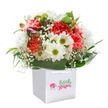 A sense of celebration pulses through this cheerful bouquet, lovingly arranged and displayed in an immaculate white gift bag-ready to brighten a home on Hurst Road or a gathering at Hall Place. Coral and peach carnations, their petals deeply ruffled and plush, infuse the display with a warm exuberance reminiscent of spring blossoms along the pavements of Bexley. Shining white daisies, marked by vivacious lime-green centers, add an uplifting contrast and a dose of lighthearted joy, recalling the buzz of neighbours gathering at local community events. Wispy clouds of baby's breath meander through the flowers, imparting a gentle softness and a sense of new beginnings. Subtle hints of purple-tinged buds peek through on one side, promising more beauty yet to unfold. Wrapping the arrangement in a loving embrace, generous loops of broad green foliage ground the bouquet, providing stability and depth. Atop the gift bag, white ribbon handles arch gracefully, suggesting the ease with which this floral harmony can make the journey to a doorstep anywhere in Bexley. Photographed against a pure white background that radiates clarity and freshness, the bouquet stands as a testament to the heartfelt effort and creativity of Bexley's local florists-a perfect gift to mark an anniversary, toast a new chapter, or simply lift someone's spirits.
