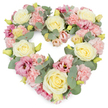 A beautifully composed heart-shaped funeral tribute is set against a plain white background, allowing its delicate pastel tones to take centre stage. The heart is fully and evenly packed with flowers, giving it a lush, generous appearance that feels protective and warm. Cream and pale yellow roses create the main structure, each bloom with tightly layered petals that form elegant, rounded heads. Between these roses, soft pink carnations nestle in clusters, their frilled petals overlapping in gentle waves and adding a comforting softness to the design. Deeper shades of mauve and magenta-pink lisianthus are scattered throughout, their slightly flared, trumpet-shaped blooms adding depth and drawing the eye along the curve of the heart. Cool, silvery-green eucalyptus leaves thread through the arrangement, their round shapes and muted colour soothing the overall palette and giving the tribute a calm, steady presence. Tiny yellow-green buds hint at unopened flowers, adding a quiet sense of renewal even in a moment of farewell. The heart shape is clearly defined and symmetrical, symbolising love, devotion, and an unbroken bond with the person being remembered. This kind of wreath would be a fitting choice for a funeral or memorial in Bexley, perhaps resting by the altar, on a stand beside the coffin, or by a framed photograph at a celebration of life. Its blend of cream, pink, and green conveys tenderness and peace, offering a gentle, floral way to say goodbye and to surround a memory with beauty and care.